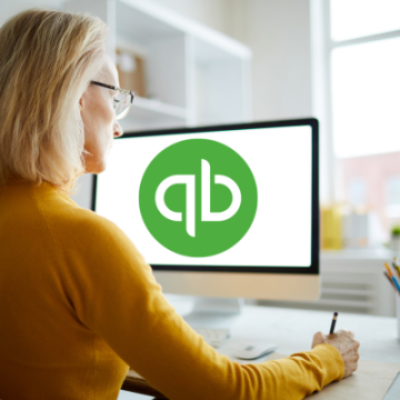 woman in yellow with computer screen and quickbooks logo on screen